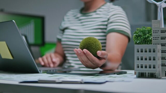 Businesswoman holding a green globe, ESG concept (Environmental, Social, and Governance), reviewing ESG reports and green financial charts, sustainability, love the earth, and eco-friendly.