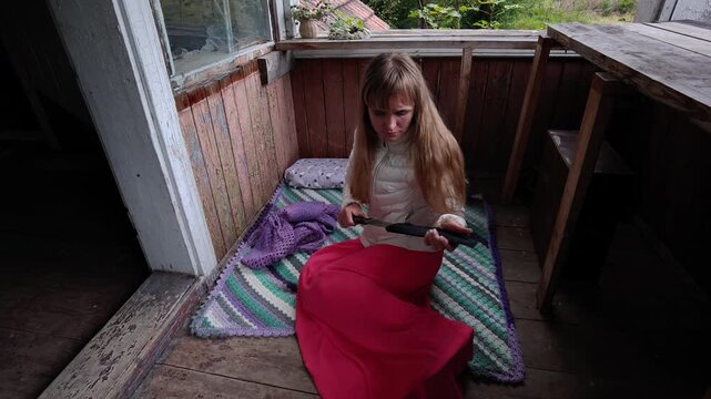 Woman inspects a knife from its sheath and hides it under blanket.