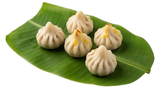 Steamed Ukadiche Modak traditional Indian sweet dumpling for Ganesh Chaturthi festival served on a fresh green banana leaf isolated on white background