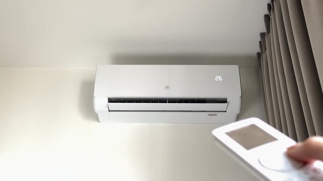 Air conditioner turned on with remote control to increase indoor room temperature parameters. Wireless controller button click changes residential split system climate settings for winter seasonal