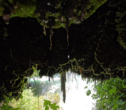 Waterfall flowing in front of a moss-covered cave