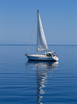 Glassy Reflection of Sailboats on Tranquil Teal Waters at Sunset, Capturing a Serene Coastal Scene