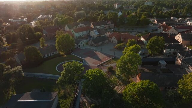 Saldus town center with circular plaza at sunset from drone, Latvia. 4K aerial footage flying over renovated round public square, historic houses, red tiled roofs, trees and streets of Saldus, Latvia.