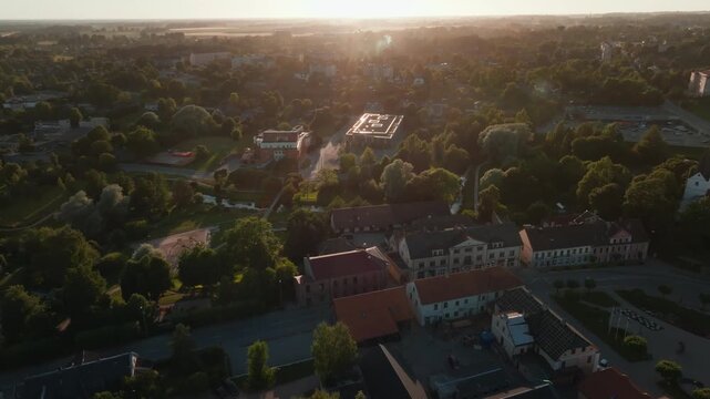 Small town and modern school with green roof from drone at sunset. 4K aerial footage crossing historic houses, red tiled roofs.
