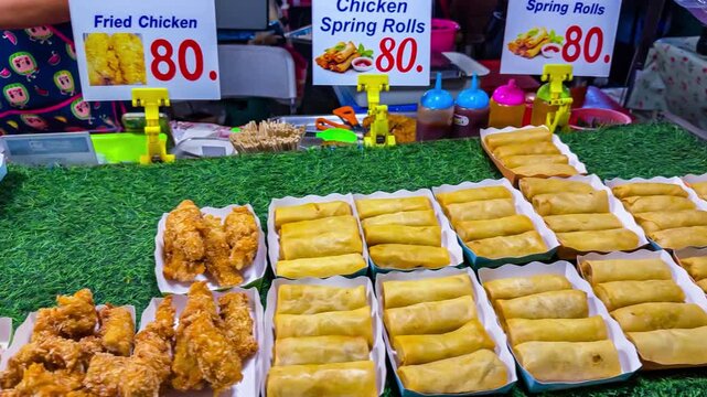 Crispy fried chicken and golden spring rolls displayed at a colorful street food market stall.