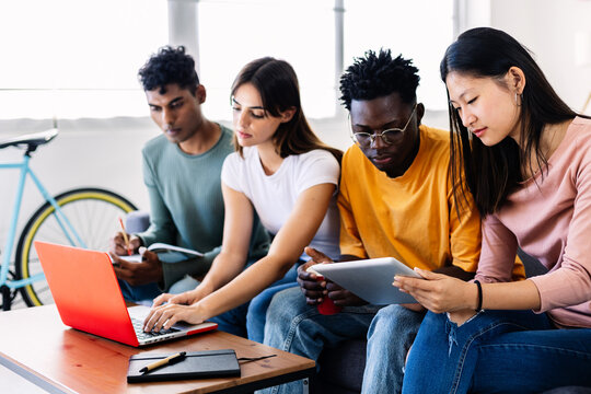 Group of diverse friends studying together with a laptop and tablet at home. Young multiracial students collaborating on a project. Friendship and teamwork concept.