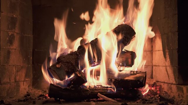 Burning wooden logs with flames and hot glowing embers inside a home fireplace. Cozy winter atmosphere and warm fire indoors.