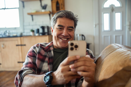 Smiling man using smartphone on sofa at home