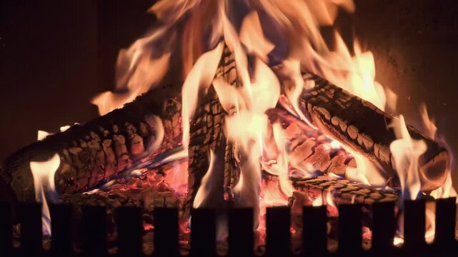 Burning wooden logs with flames and hot glowing embers inside a home fireplace. Cozy winter atmosphere and warm fire indoors.