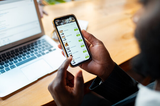 Person ordering coffee on smartphone next to laptop