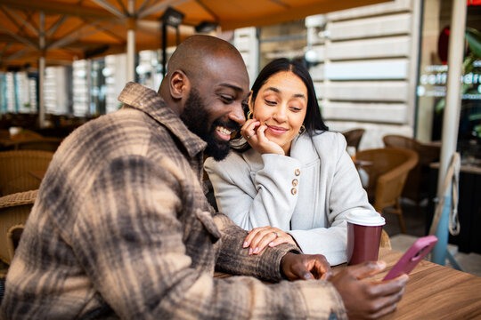 Couple laughing over a smartphone at an outdoor cafe