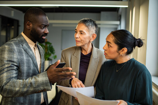 Man explaining as coworkers review paperwork in office