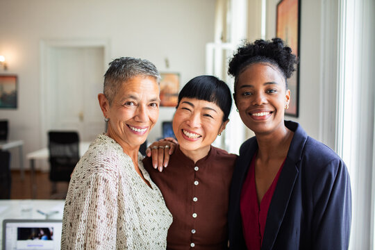 Three smiling coworkers with arms around each other in office