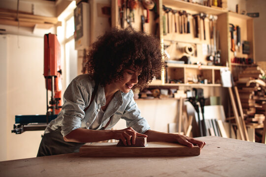 Woman sanding wooden board in a carpentry workshop