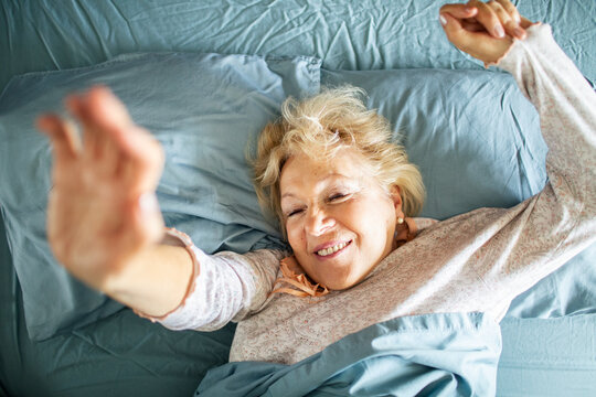 Smiling senior woman stretching in bed after waking