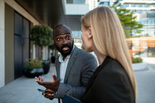 Coworkers talk as man gestures with smartphone outside office