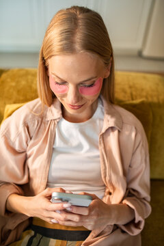 Woman with under-eye patches texting on sofa at home