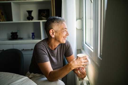 Smiling older woman with coffee by the window