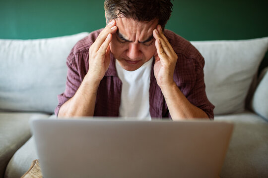 Man rubbing temples in front of laptop at home