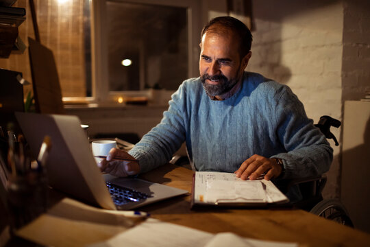 Man in wheelchair working on laptop with planner at home
