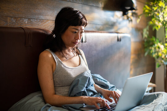 Woman typing on laptop in bed at home