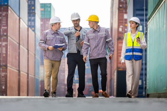 Team of engineers and logistics workers walking and discussing operations in container yard, diverse group of colleagues reviewing logistics data outdoors among freight containers