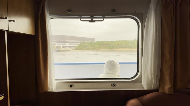 A traveler in a white jacket looks out a cabin window at the Neva River. The cozy framing brings a calm and peaceful feeling.