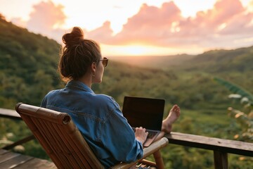 Obraz premium Woman using laptop on balcony overlooking tropical valley at sunset, rear view
