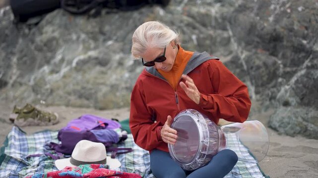 A mature woman plays the drum on the beach in Fort Bragg, California, enjoying a sunny day by the ocean.