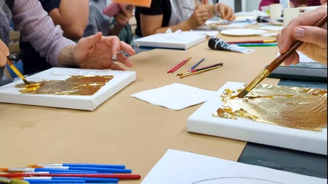 Women apply gold leaf on canvas during art workshop. Hands gilding painting with brush in gold leaf workshop masterclass.