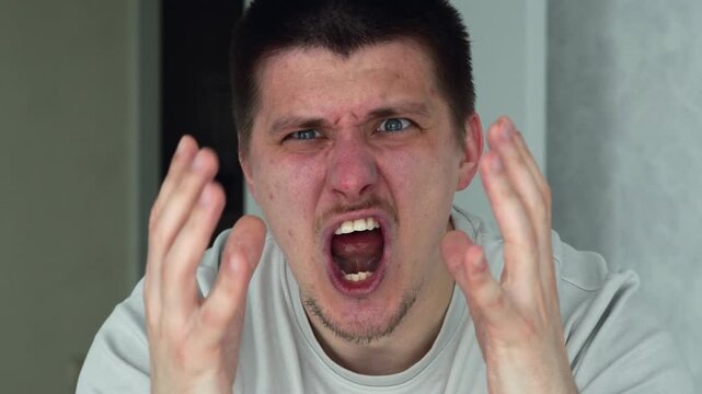 A man standing in a brightly lit room, showing angry emotions.
The man is agitated and shouting.