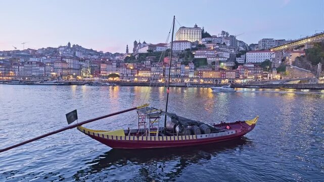 Sunset rabelo boat on the Douro River by Porto Ribeira, Portugal, with twilight color and Vila Nova de Gaia lights across the water