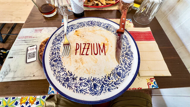  Empty ceramic plate bearing the PIZZIUM brand name with a fork and knife resting on a rustic wooden table after a meal in a charming Italian restaurant ideal for hospitality themes