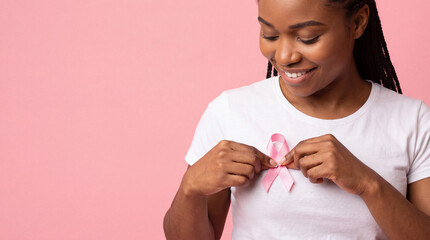 Fototapeta premium Smiling woman wearing pink ribbon on white shirt against pink background for breast cancer awareness portrait
