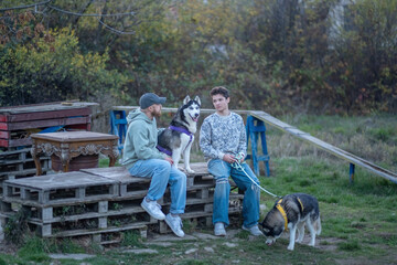 Man and teenage son sit on pallet steps with husky between them, parenting through shared hobby instead of lectures, moment building real trust. Wide shot. Concept of parenting through shared hobby © iwavephoto