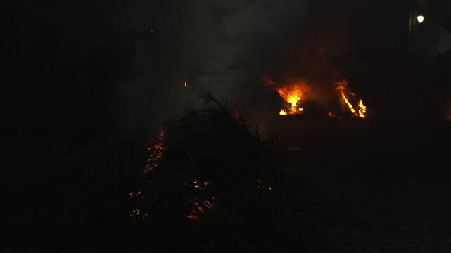 Traditional bonfire burning brightly during a cultural festival at night. Silhouettes of people are gathering around the large flames and smoke