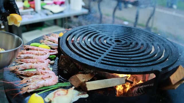 Fresh shrimp grilling on round charcoal barbecue with flames and smoke. Seafood cooking on grill with zucchini at street food stall. Delicious prawns preparation closeup