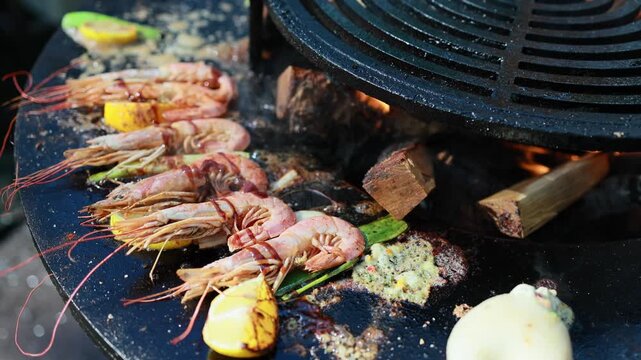Shrimp grilling on round charcoal grill with lemon slices and garlic sauce. Barbecue seafood cooking over burning wood and coals, outdoor summer food preparation concept.