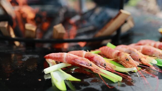 Fresh prawns with green onion cooking on hot black grill plate. Seafood barbecue preparation outdoors. Grilled shrimp with leek stems, healthy food and street food concept.