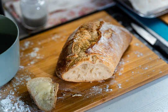 Fresh homemade bread loaf with a buttered slice on a wooden board