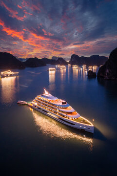 Aerial view of illuminated cruise ships anchored in Ha Long Bay, Vietnam, at dusk with dramatic sunset clouds and limestone karsts