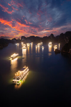 Aerial view of illuminated cruise ships anchored in Ha Long Bay, Vietnam, at dusk with dramatic sunset clouds and limestone karsts