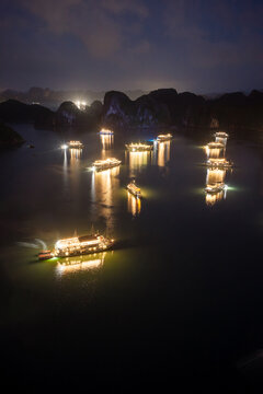 Aerial view of illuminated cruise ships anchored in Ha Long Bay, Vietnam, at dusk with dramatic sunset clouds and limestone karsts