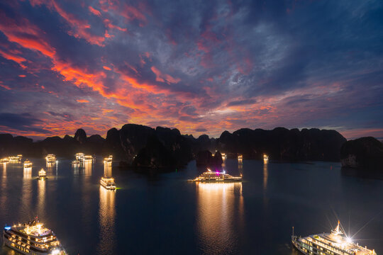 Aerial view of illuminated cruise ships anchored in Ha Long Bay, Vietnam, at dusk with dramatic sunset clouds and limestone karsts