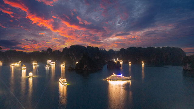 Aerial view of illuminated cruise ships anchored in Ha Long Bay, Vietnam, at dusk with dramatic sunset clouds and limestone karsts