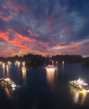 Aerial view of illuminated cruise ships anchored in Ha Long Bay, Vietnam, at dusk with dramatic sunset clouds and limestone karsts