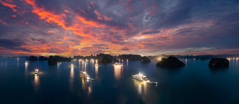 Aerial view of illuminated cruise ships anchored in Ha Long Bay, Vietnam, at dusk with dramatic sunset clouds and limestone karsts