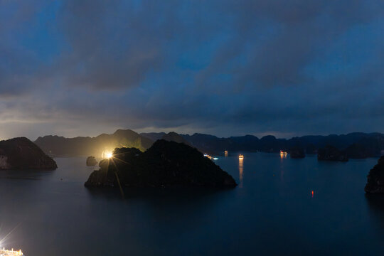 Aerial view of illuminated cruise ships anchored in Ha Long Bay, Vietnam, at dusk with dramatic sunset clouds and limestone karsts