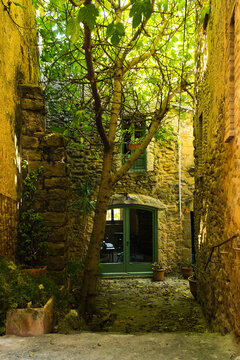 Patio estrecho de piedra con un &aacute;rbol central y edificios r&uacute;sticos alrededor
