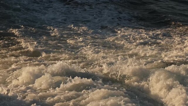 Gentle waves spread outward across the ocean as a boat moves through the water, creating a beautiful pattern of ripples and foam that slowly expands across the calm surface.